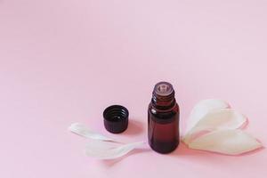 Bottle with aromatic oil and flower petals on pink background. photo