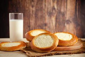 Buns with cottage cheese and glass of milk on wooden background. photo