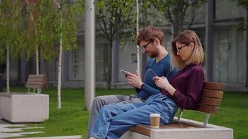 Two friends using smartphones outdoor park. video