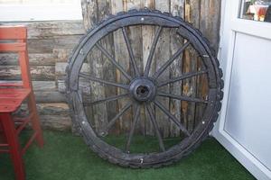 Forgotten old Wooden Wagon Wheel Leaning Against a wooden Wall. Cartwheels at the old wood wall of the house. photo