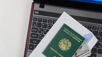 pasaporte de uzbekistán con dólares estadounidenses en el teclado de la computadora portátil. Registro en línea. concepto - soborno y corrupción. vista superior foto