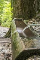 Jet of fresh spring water coming out of a metal spout from a stone fountain in Austrian mountains. photo