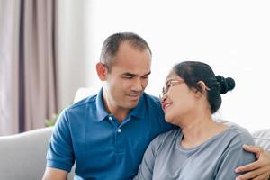 retrato de una pareja madura asiática sentada en la sala de estar. esposa y esposo abrazándose, tomados de la mano con felicidad y alegría. concepto de familia de amor, seguridad y seguros foto