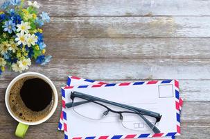 Top view with air mail envelope,cup of coffee,glasses and flower on wood table background. photo