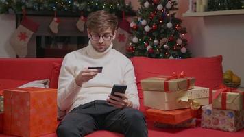 el hombre hace una compra en línea usando un teléfono inteligente y una tarjeta de crédito, compra regalos de navidad en internet. video