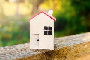 casa modelo de juguete blanco en miniatura con fondo de madera cerca de fondo verde. aldea ecológica, fondo ambiental abstracto. concepto de ecología de casa de ensueño de seguro de propiedad de hipoteca de bienes raíces. foto