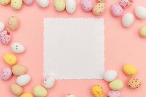 Happy Easter concept. Candy chocolate eggs and jellybean sweets with mockup empty poster isolated on pastel pink background. Simple minimalism flat lay top view copy space. photo
