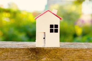 casa modelo de juguete blanco en miniatura con fondo de madera cerca de fondo verde. aldea ecológica, fondo ambiental abstracto. concepto de ecología de casa de ensueño de seguro de propiedad de hipoteca de bienes raíces. foto