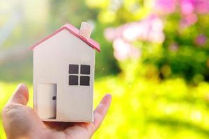 Miniature model house in female woman hand on green outdoor background. Eco Village, abstract environmental background. Real estate mortgage property insurance dream home ecology concept. photo