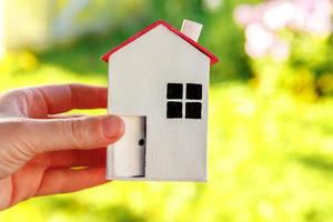 casa modelo en miniatura en mano de mujer sobre fondo verde al aire libre. aldea ecológica, fondo ambiental abstracto. concepto de ecología de casa de ensueño de seguro de propiedad de hipoteca de bienes raíces. foto