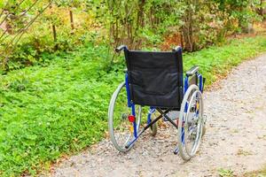 Empty wheelchair standing on road in hospital park waiting for patient services. Invalid chair for disabled people parked outdoor in nature. Handicap accessible symbol. Health care medical concept. photo