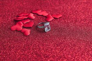 Will you marry me. Wedding ring and many red hearts on red glitter background. Engagement marriage proposal wedding concept. St. Valentine's Day postcard. Banner on valentines day.