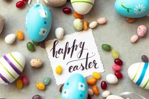 Happy Easter concept. Preparation for holiday. Easter eggs Inscription HAPPY EASTER letters candy chocolate eggs and jellybean sweets on concrete stone grey background. Flat lay top view copy space. photo