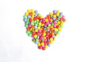 En forma de corazón un montón de coloridos caramelos recubiertos de chocolate aislado sobre fondo blanco. foto