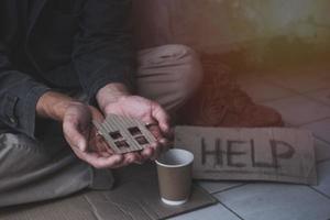 Homeless adult man sitting on the street in the shadow of the building and begging for help and money with sign.  Homeless concept. photo