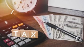 Debt collection and tax season concept. The word tax written in wooden block letters with calculator, money, clock, pen, background, Time to pay concept photo