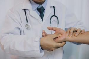 médico revisando el dolor de la mano del paciente. primer plano de un hombre caucásico, con una bata blanca, moviendo la mano de un paciente caucásico mayor. foto