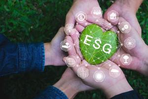 Adult hands holding green heart with ESG icon concept for environmental, social, and governance in sustainable and ethical business on the Network connection on a green background. photo