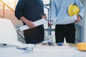 Builder two asian young engineer man construction site engineer. Engineering objects on workplace with partners interacting on background. Real-estate concept photo