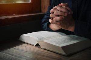 el hombre está leyendo y rezando las escrituras o la santa biblia en una mesa de madera con espacio para copiar. religión, concepto de creencia. foto