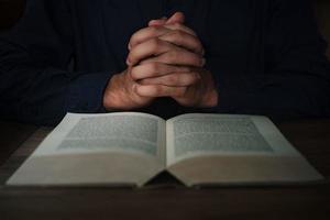 el hombre está leyendo y rezando las escrituras o la santa biblia en una mesa de madera con espacio para copiar. religión, concepto de creencia. foto