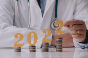 médico con uniforme blanco con el número 2022 con moneda en el escritorio del médico. feliz año nuevo para la atención médica y el concepto médico. foto