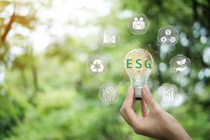 Hand holding light bulb with ESG icon concept for environmental, social, and governance in sustainable and ethical business on the Network connection on a green background. photo