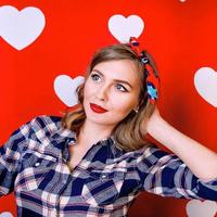 Hermosa mujer joven en estilo pin-up en rojo con fondo de corazones blancos foto