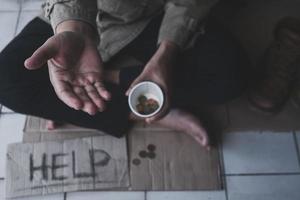 Homeless adult man sitting on the street in the shadow of the building and begging for help and money with sign.  Homeless concept. photo