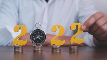 Man hands putting gold wooden number 2022 on the stack of coins compass, financial direction 2022. Tax payment, 2022 new year saving money and financial planning concept photo