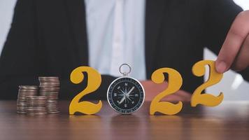 Man hands putting gold wooden number 2022 on the stack of coins compass, financial direction 2022. Tax payment, 2022 new year saving money and financial planning concept photo