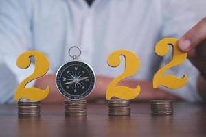 Man hands putting gold wooden number 2022 on the stack of coins compass, financial direction 2022. Tax payment, 2022 new year saving money and financial planning concept photo