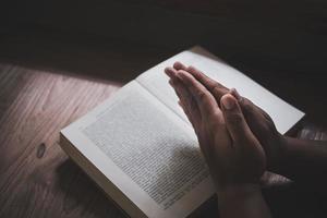 Man with Bible praying, hands clasped together on her Bible on wooden table. photo