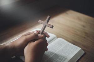 Man holding wooden cross in hands on bible and divine light. Religion concept. photo