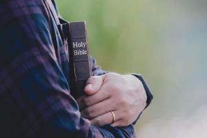 hombre en espera y abrazando la sagrada biblia en el banco. cristiano orando creer concepto. foto