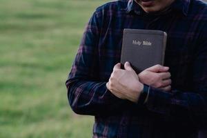 hombre en espera y abrazando la sagrada biblia en el banco. cristiano orando creer concepto. foto