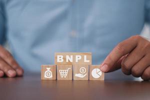 Businessman pressing his finger on the wooden cubes with BNPL with online shopping icons. BNPL Buy now pay later online shopping concept. photo