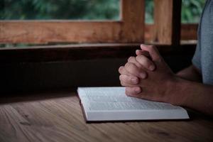 Man with Bible praying, hands clasped together on her Bible on wooden table. photo