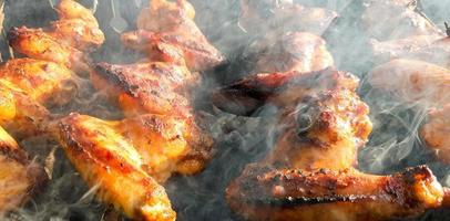 Delicious juicy grilled chicken wings outdoors in smoke. BBQ Chicken Cooking Process photo