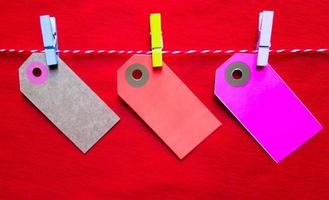Colorful paper notes and clothespins on a red background. Empty color cardboard price tags, sale tag, gift tag, address label, luggage label hanging on clothes. Wooden clips. photo