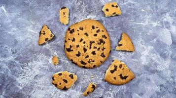 One soft freshly baked chocolate chip cookie with crumbs and chunks on a gray marble kitchen countertop. American traditional pastry, dessert. Delicious sweet food. Flat lay. photo