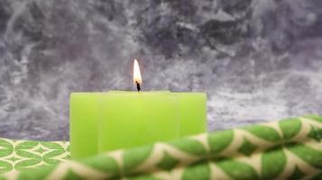 Composition with one green lit candle on a table with a green linen napkin against a beautiful gray marble background. Place for your text. Christmas decorations. photo