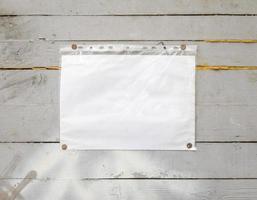 White paper sign with rivets, vintage background on a gray wooden old backdrop. Wooden textured wall, weighs a white blank cardboard sign lit by the sun, closeup photo