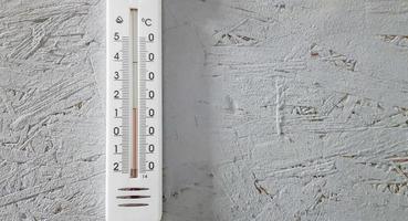 white thermometer hanging on a gray gray wooden wall indoors, background with copy space and empty place for your text photo