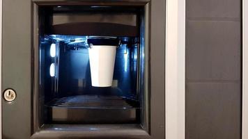 vaso de papel blanco en la ventana de una máquina expendedora de café. el proceso de hacer cafe en una vadeadora foto