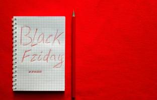 Black friday sale text written on a notepad with a red pencil on a red background. Background, holiday concept. Black Friday - International Day of Shopping, Promotions, Discounts, Sales. photo