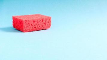 One red sponge on a blue background is used to wash and erase the dirt used by housewives in everyday life. They are made of porous material. Saving detergent, which allows you to use it sparingly photo