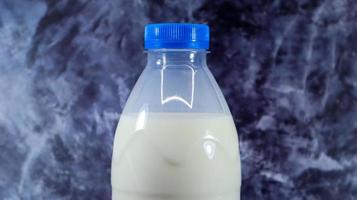 A plastic bottle with a blue cap of fresh regular milk on a dark gray marbled or concrete background. Close-up front view. World milk day concept. Nutrient fluid. photo