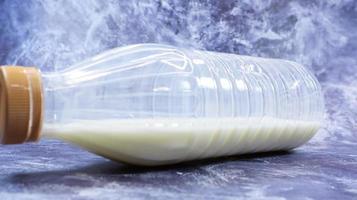 A semi-empty plastic bottle of fresh regular milk lies on a dark gray marble or concrete backdrop. Close-up front view. World milk day concept. Nutrient fluid. photo