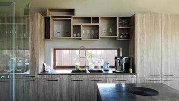 Ukraine, Kiev - September 24, 2019. Modern kitchen with brown wooden furniture, stone countertops, sink and faucet. A coffee machine is on the table. Interior, kitchen design in a big house. photo